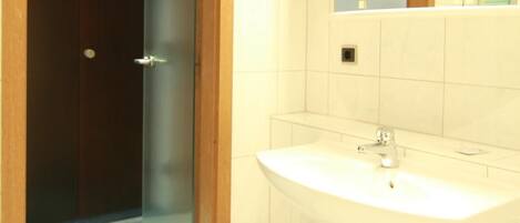 A bathroom with a white sink, a mirror, and a door leading to a shower area.