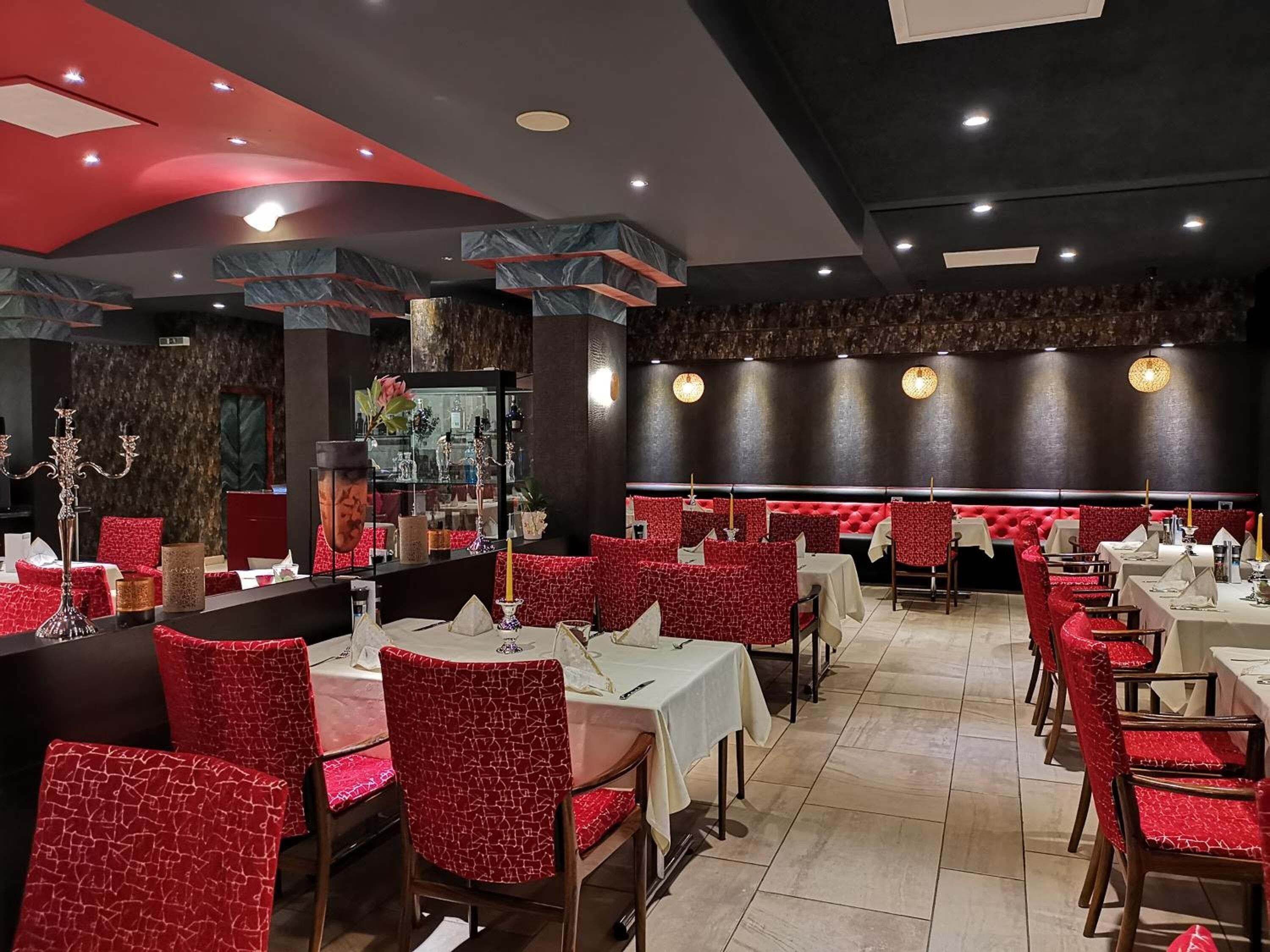 A restaurant with red upholstered booths and tables, marble accents on the ceiling, and a dark wall with a textured pattern.