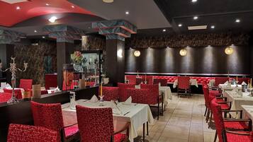 A restaurant with red upholstered booths and tables, marble accents on the ceiling, and a dark wall with a textured pattern.