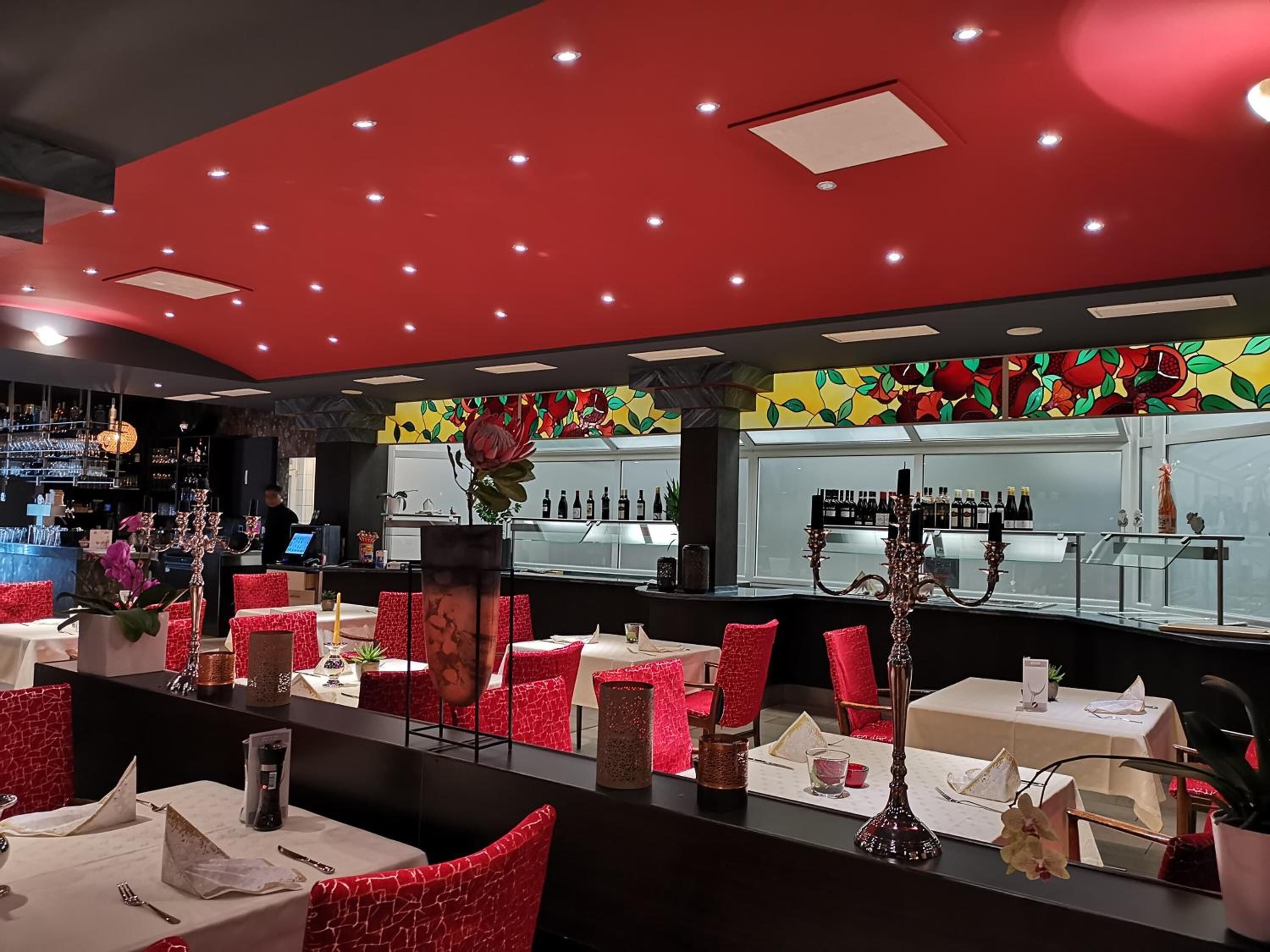 A restaurant with red chairs, tables, and a bar area with shelves of bottles.