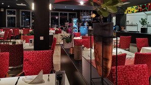 A restaurant with red patterned chairs, a large flower centerpiece, and a bar area in the background. - Hotel Restaurant Pfeffermühle (Balingen)