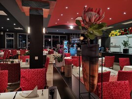 Un restaurante con sillas rojas con estampado, un gran centro de mesa floral y una zona de bar al fondo.