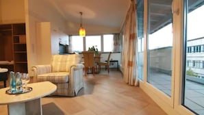 A spacious living room with a sofa, a dining table, and a TV. There is a large window providing a view of the outside. - Hotel Restaurant Pfeffermühle (Balingen)