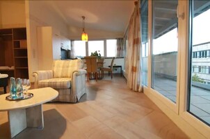 Un salón amplio con un sofá, una mesa de comedor y un televisor. Una ventana grande ofrece vistas al exterior.