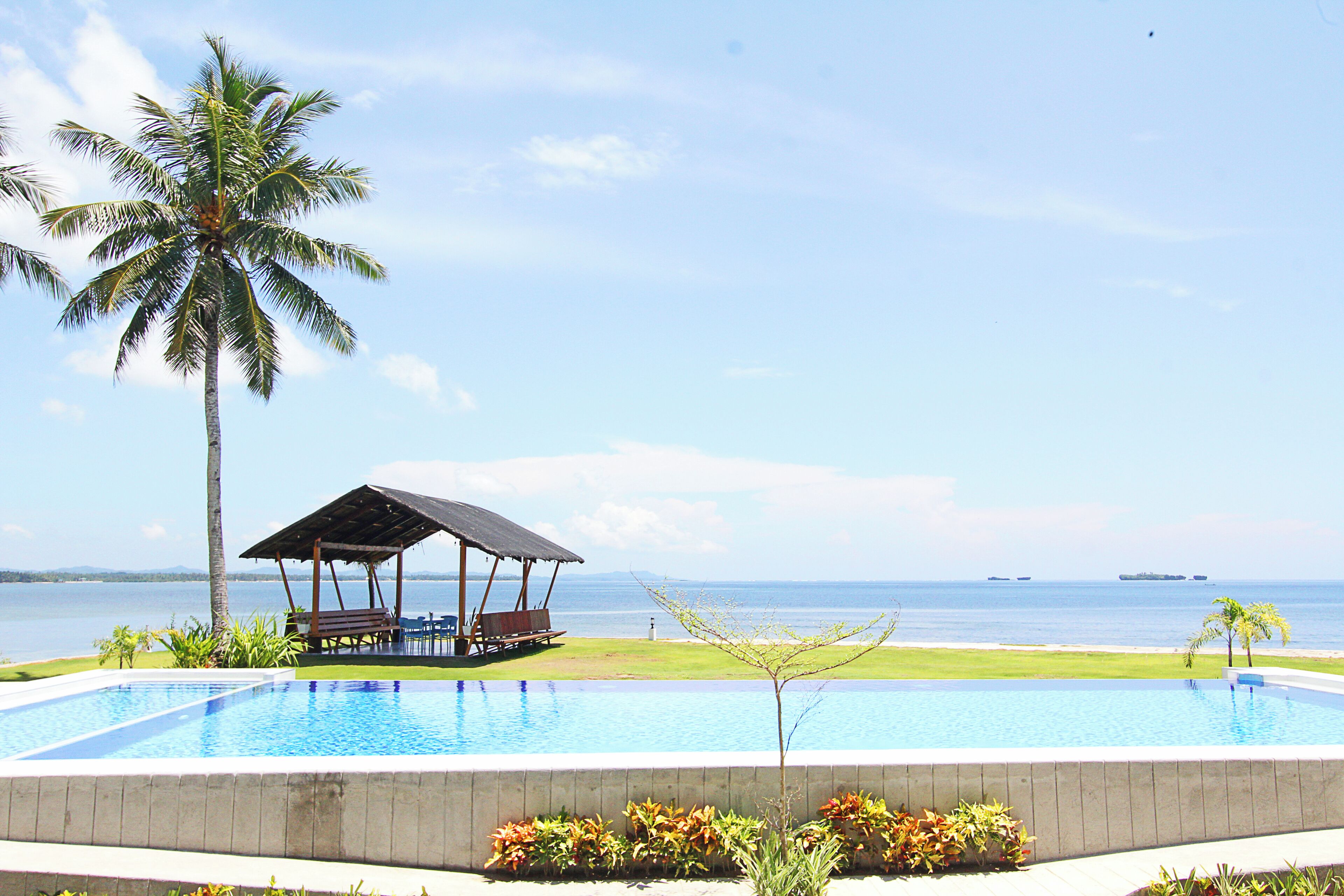 A swimming pool with a gazebo and palm trees, overlooking a body of water.