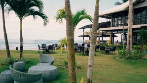 A beachfront patio with round seating, palm trees, and a view of the ocean. - Ocean 101 Beach Resort (General Luna)