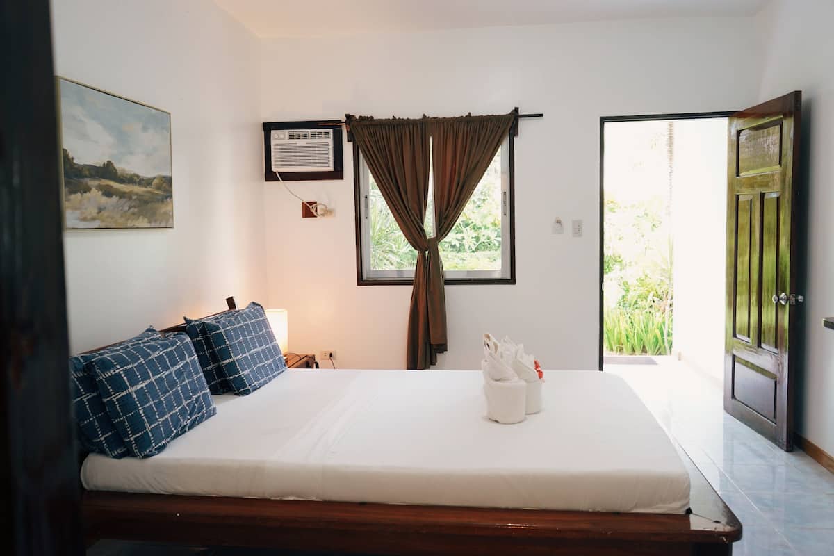 Una cama bien hecha con almohadas azules y blancas, un cuadro en la pared y una ventana con cortinas.