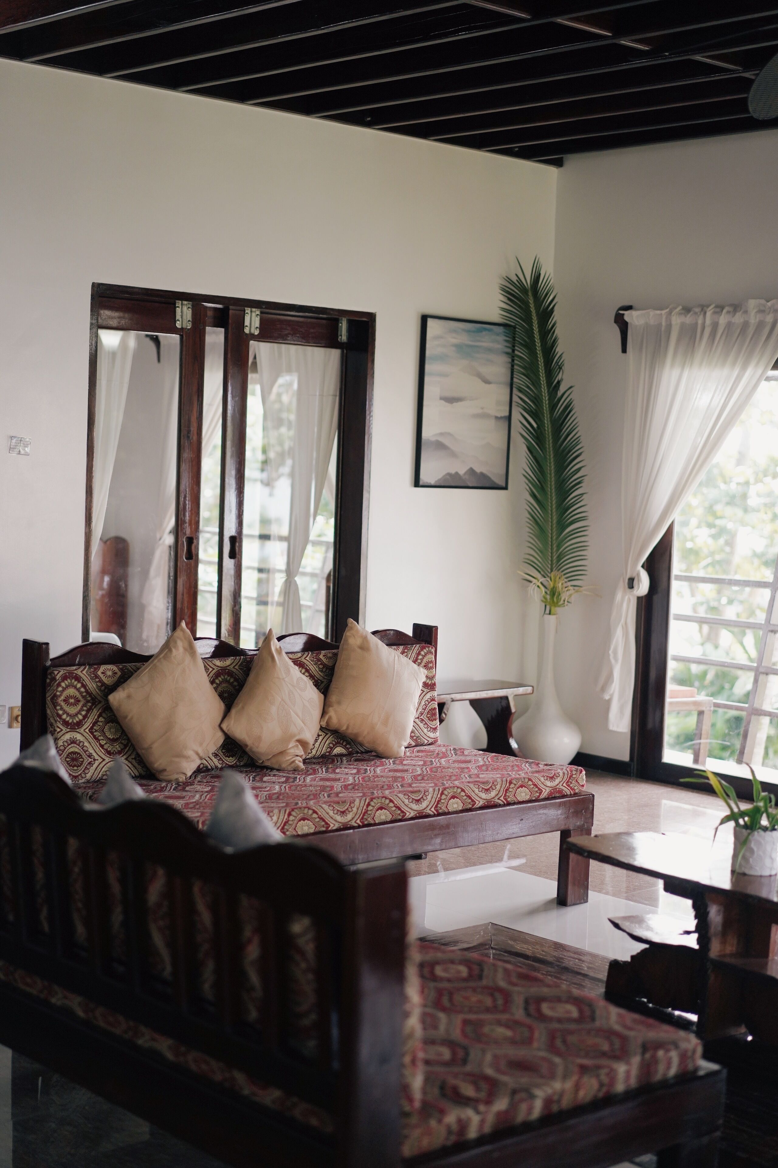 A room with a wooden sofa, a small table, a potted plant, and a window with curtains.