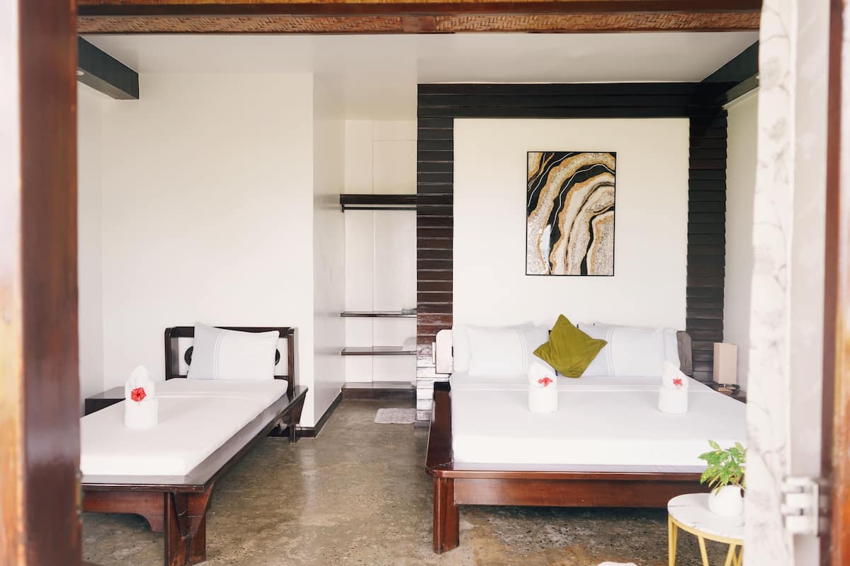 Habitación de hotel con dos camas, un cuadro abstracto de gran tamaño en la pared y una pequeña mesa redonda con una planta.