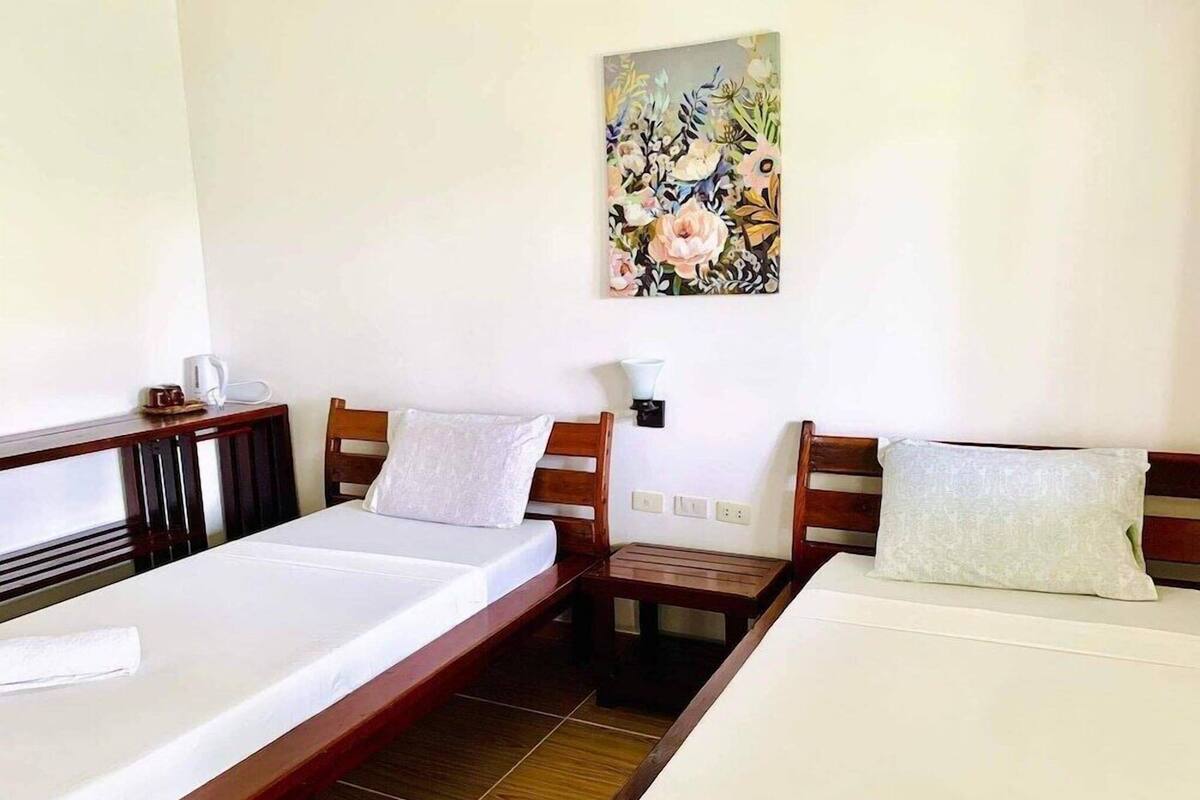 Habitación de hotel con dos camas individuales, cabecera de madera, mesita de noche con lámpara y un cuadro en la pared.