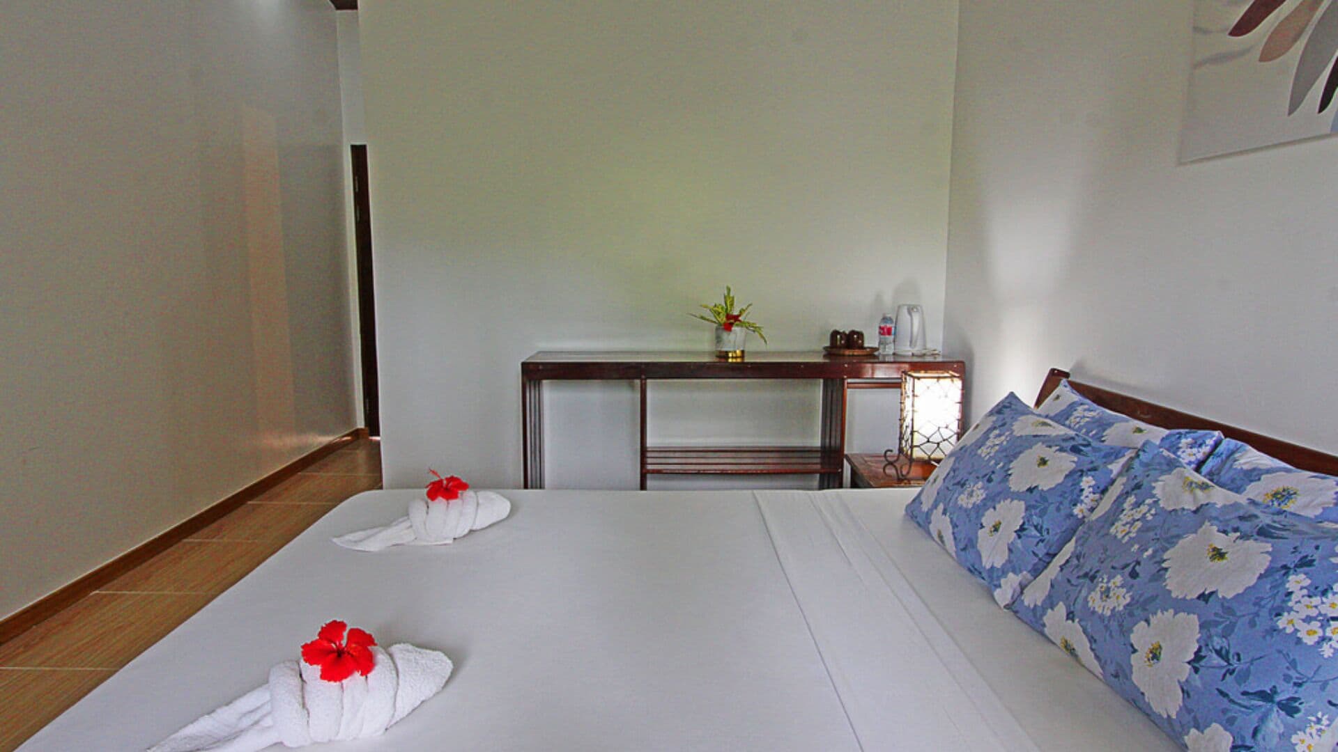Habitación de hotel con una cama, una mesita de noche, una lámpara y una pequeña mesa con una planta y una botella.