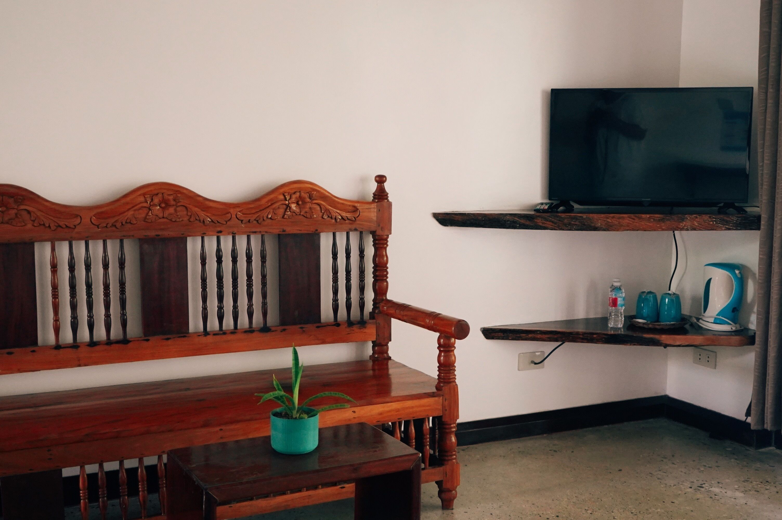 A wooden bench with a potted plant, a television on a shelf, and a kettle on a small table.