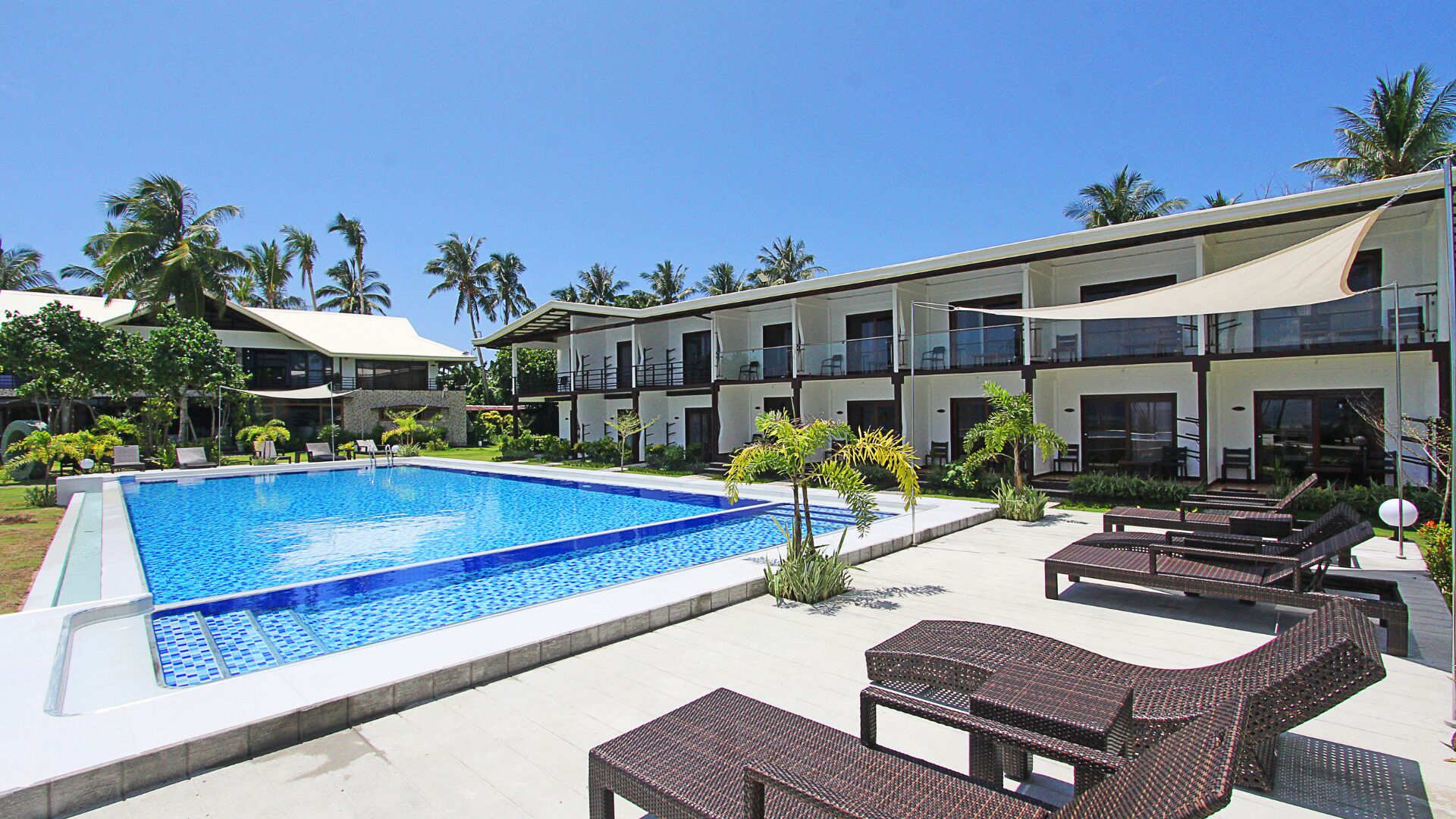 A swimming pool with lounge chairs and a building with balconies.