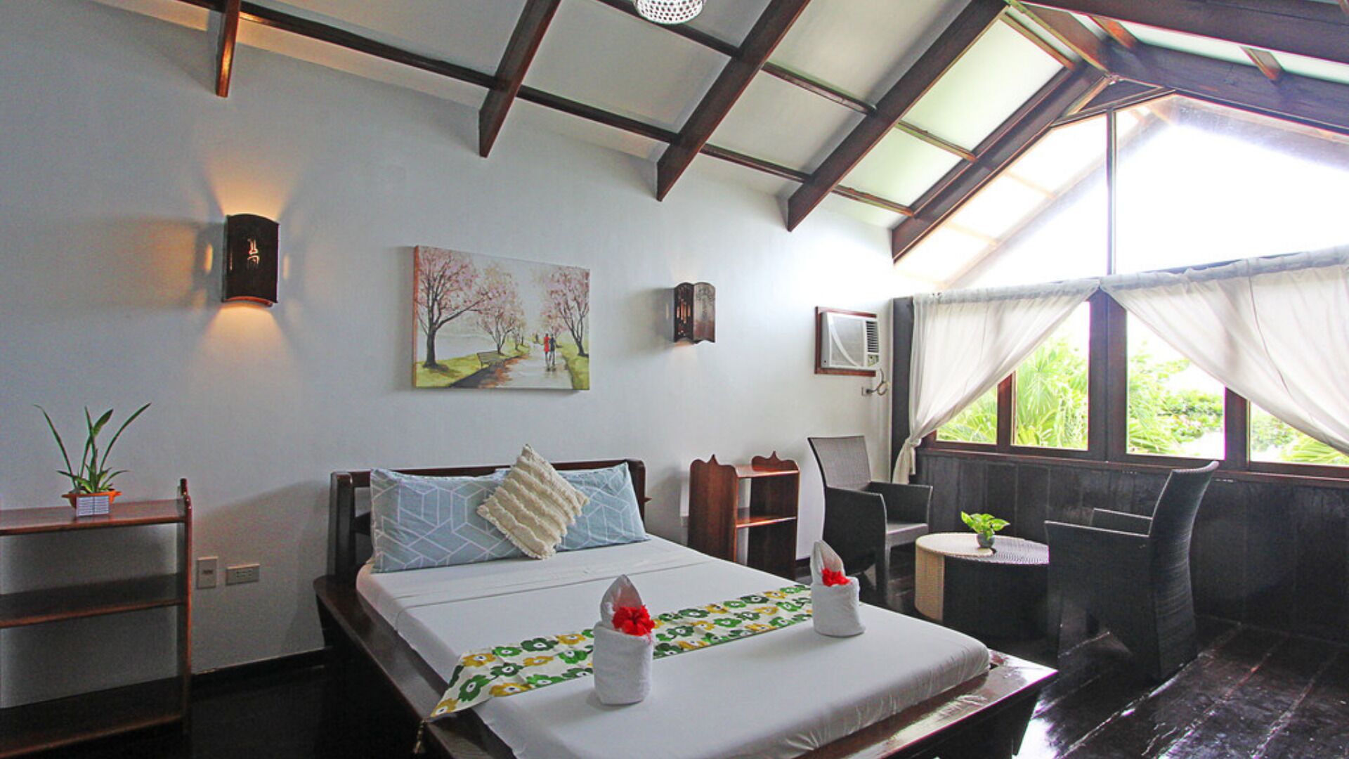 Un dormitorio con cama, mesitas de noche, un ventanal con cortinas, aire acondicionado instalado en la pared y un cuadro.