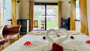 A hotel room with a bed, a wooden chair, a television, and a view of a garden through the window. - Ocean 101 Beach Resort (General Luna)