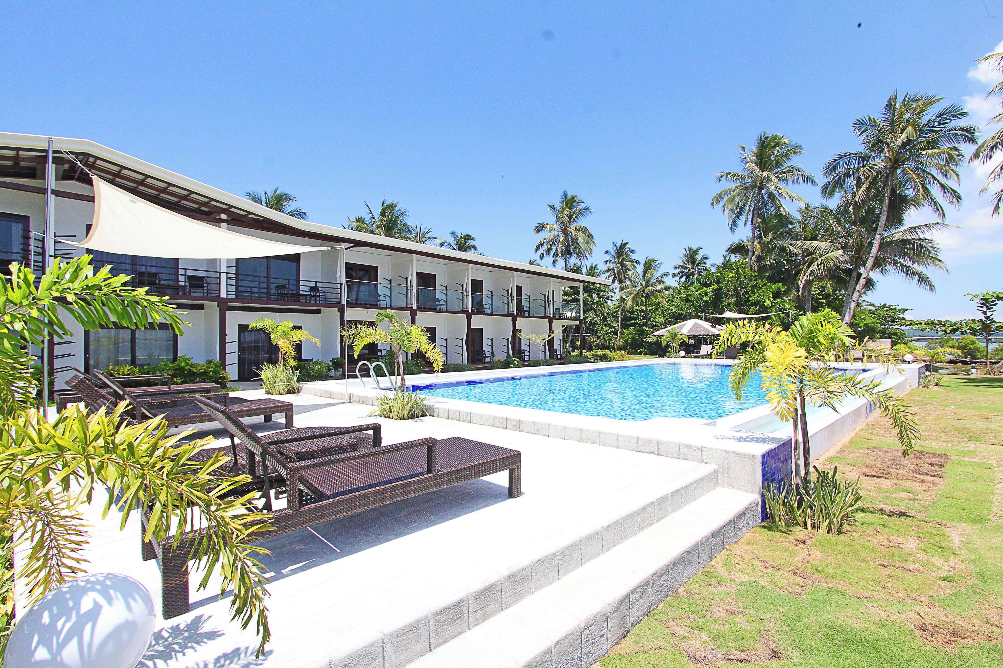 A hotel with a swimming pool, outdoor seating, and palm trees.