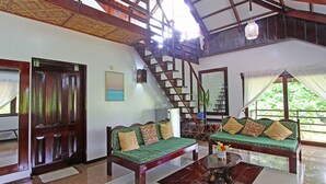 A spacious living area with a high ceiling, wooden staircase, and two green sofas with cushions. - Ocean 101 Beach Resort (General Luna)