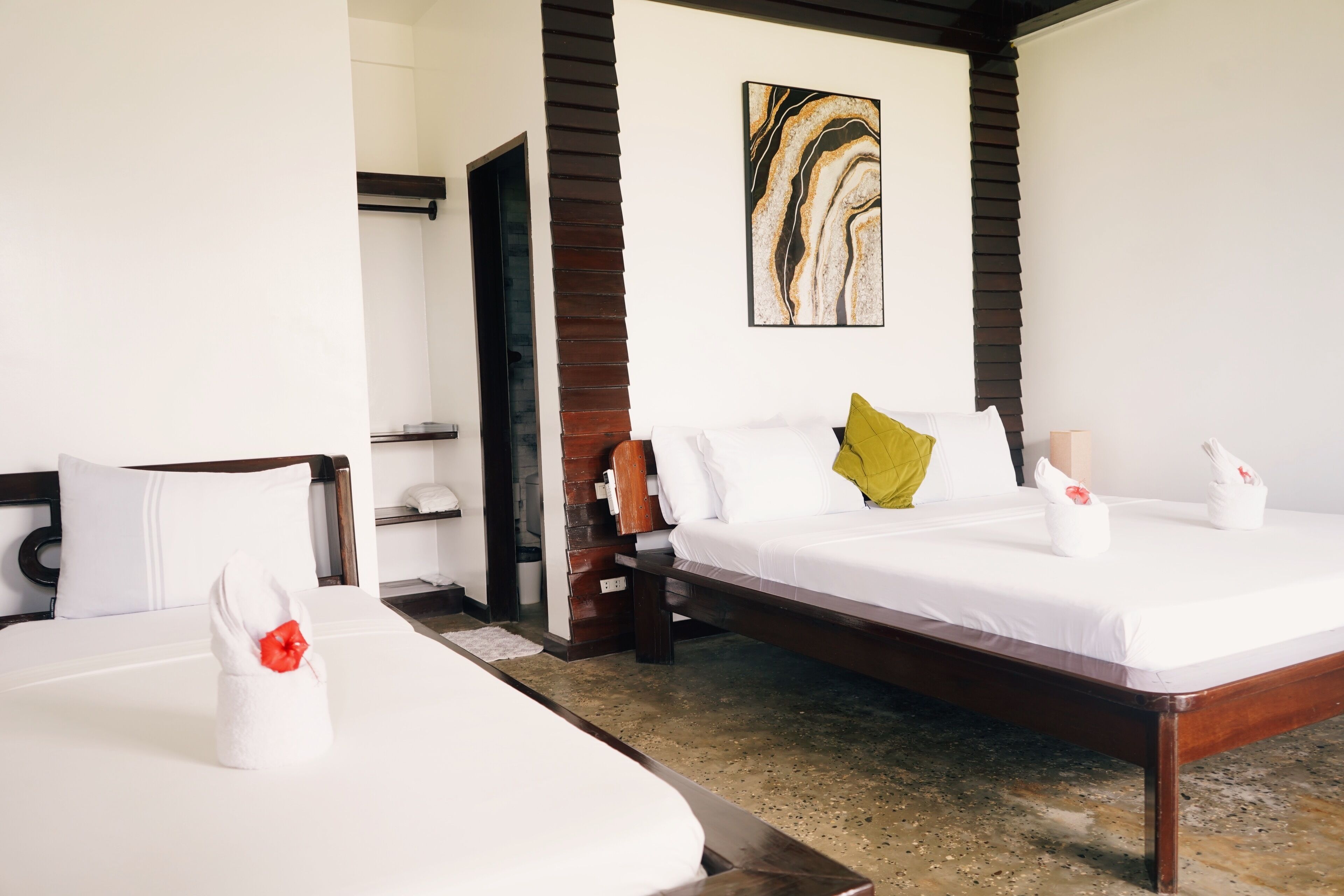 Une chambre d’hôtel avec deux lits, une tête de lit en bois, une décoration murale en marbre et une petite table avec une lampe.