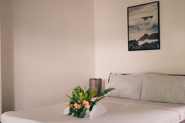 Una cama bien hecha con edredón blanco, un arreglo decorativo de plantas y un cuadro en la pared.