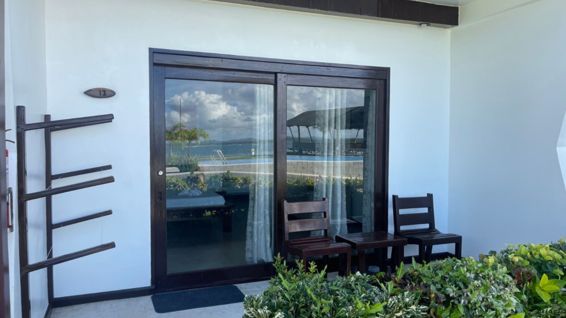 A modern building with a sliding glass door leading to a balcony with two wooden chairs and a small table.