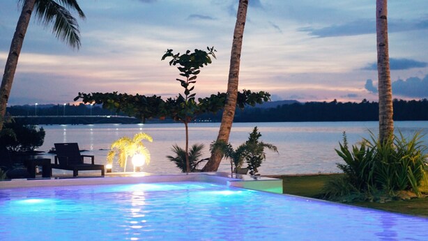 A swimming pool with a view of a lake and palm trees at dusk. - Ocean 101 Beach Resort (General Luna)