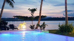 Una piscina con vista a un lago y palmeras al atardecer.