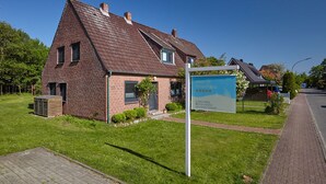 A two-story brick house with a sloped roof, a small front garden, and a signboard. - Ferienhaus Düneneck 10 (St. Peter-Ording)