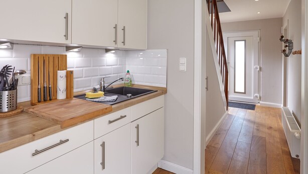 A modern kitchen with white cabinets, a wooden countertop, and a black sink. - Ferienhaus Düneneck 10 (St. Peter-Ording)