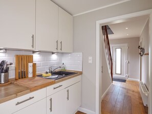 A modern kitchen with white cabinets, a wooden countertop, and a black sink. - Ferienhaus Düneneck 10 (St. Peter-Ording)