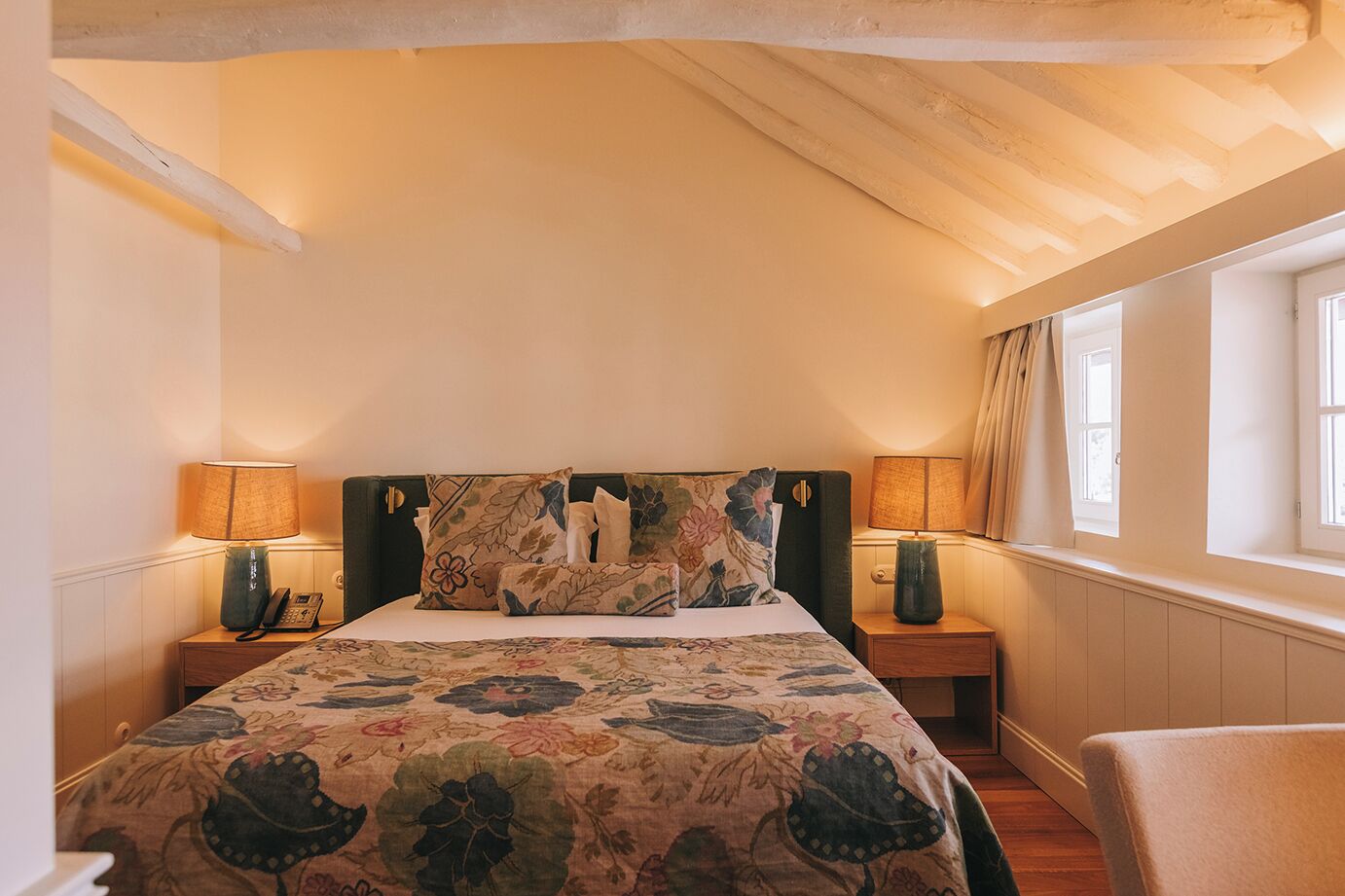 Une chambre à coucher avec un grand lit, deux lampes de chevet, un téléphone et une fenêtre avec des rideaux.