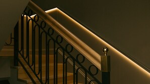 Eine Treppe mit hölzernem Geländer und schwarzen Metallspindeln, beleuchtet durch Unterbauleuchten.