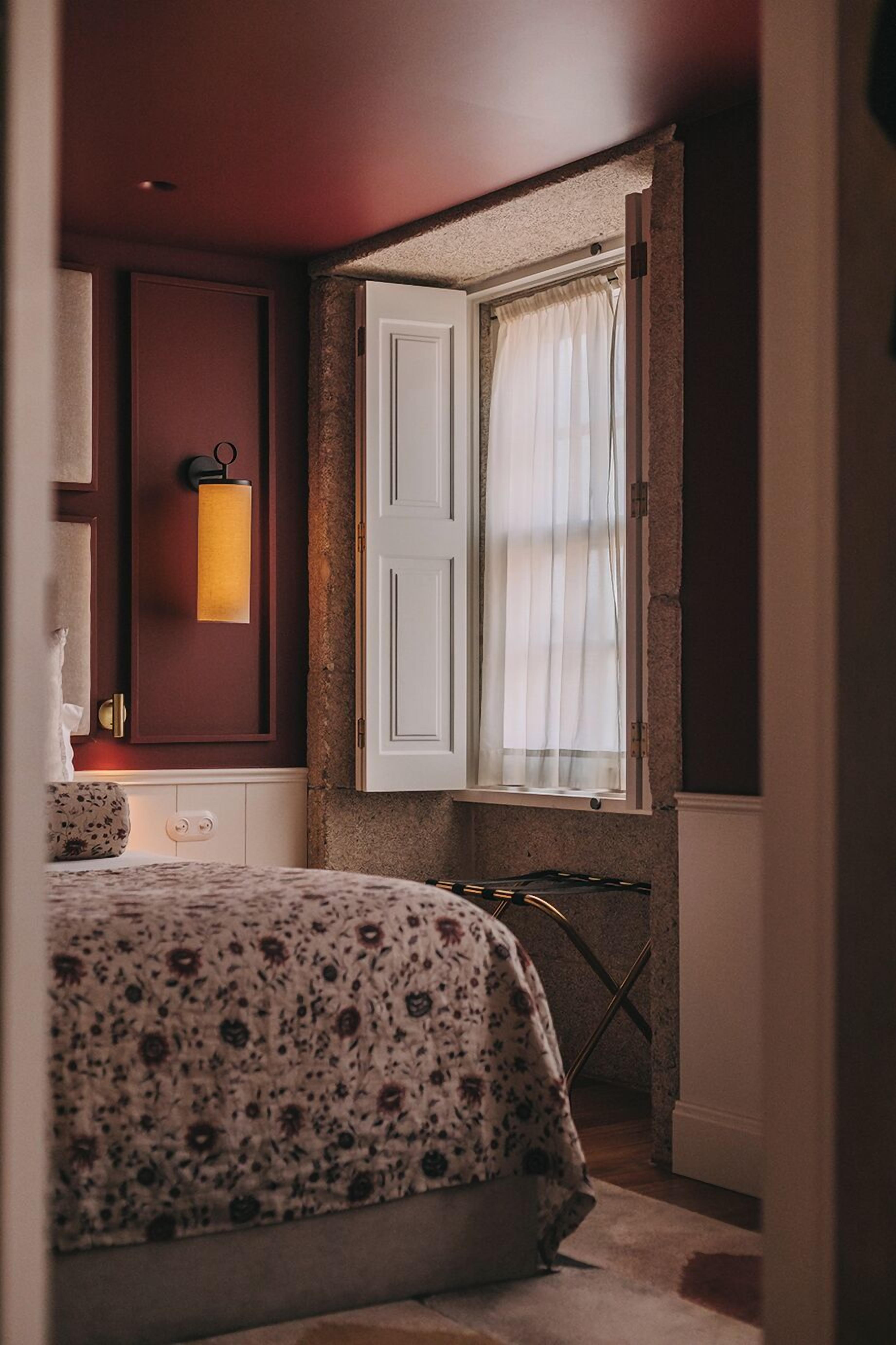A bedroom with a bed, a nightstand, a lamp, a window with curtains, and a door.