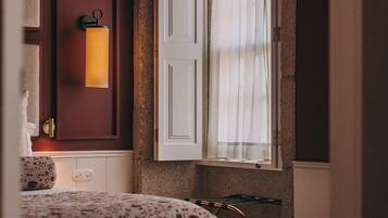 A bedroom with a bed, a nightstand, a lamp, a window with curtains, and a door.