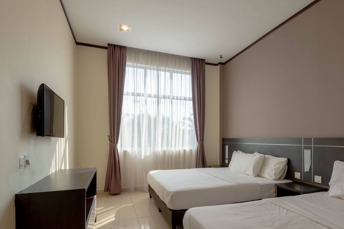 A hotel room with two beds, a TV mounted on the wall, and a large window with curtains.