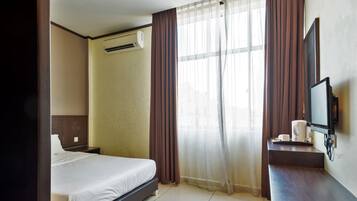 A hotel room with a bed, a TV on a stand, a coffee maker, and an air conditioning unit.
