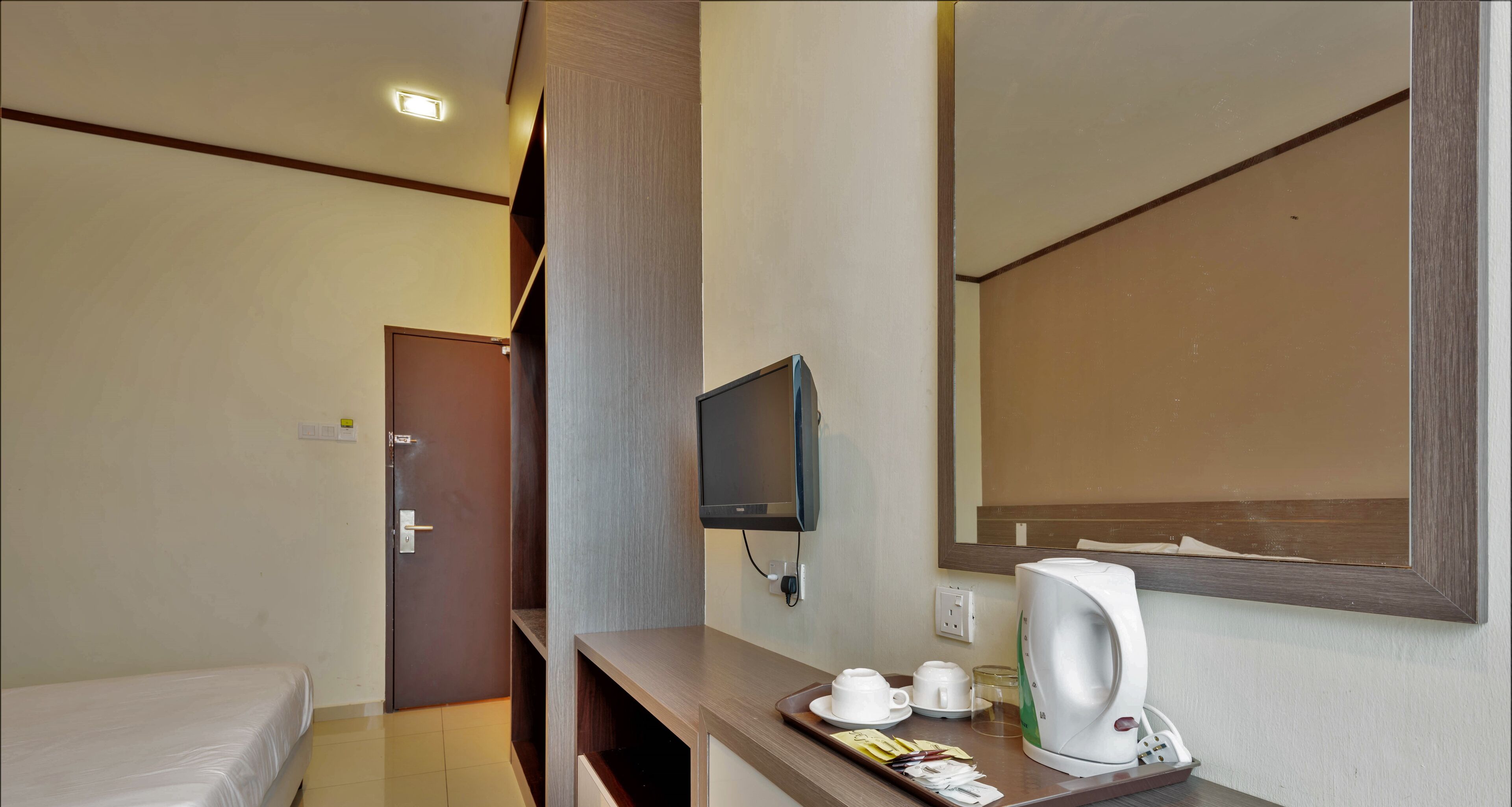 A hotel room with a bed, a TV mounted on the wall, a coffee maker, and a tray with cups and a glass.