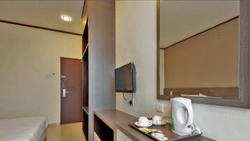 A hotel room with a bed, a TV mounted on the wall, a coffee maker, and a tray with cups and a glass.