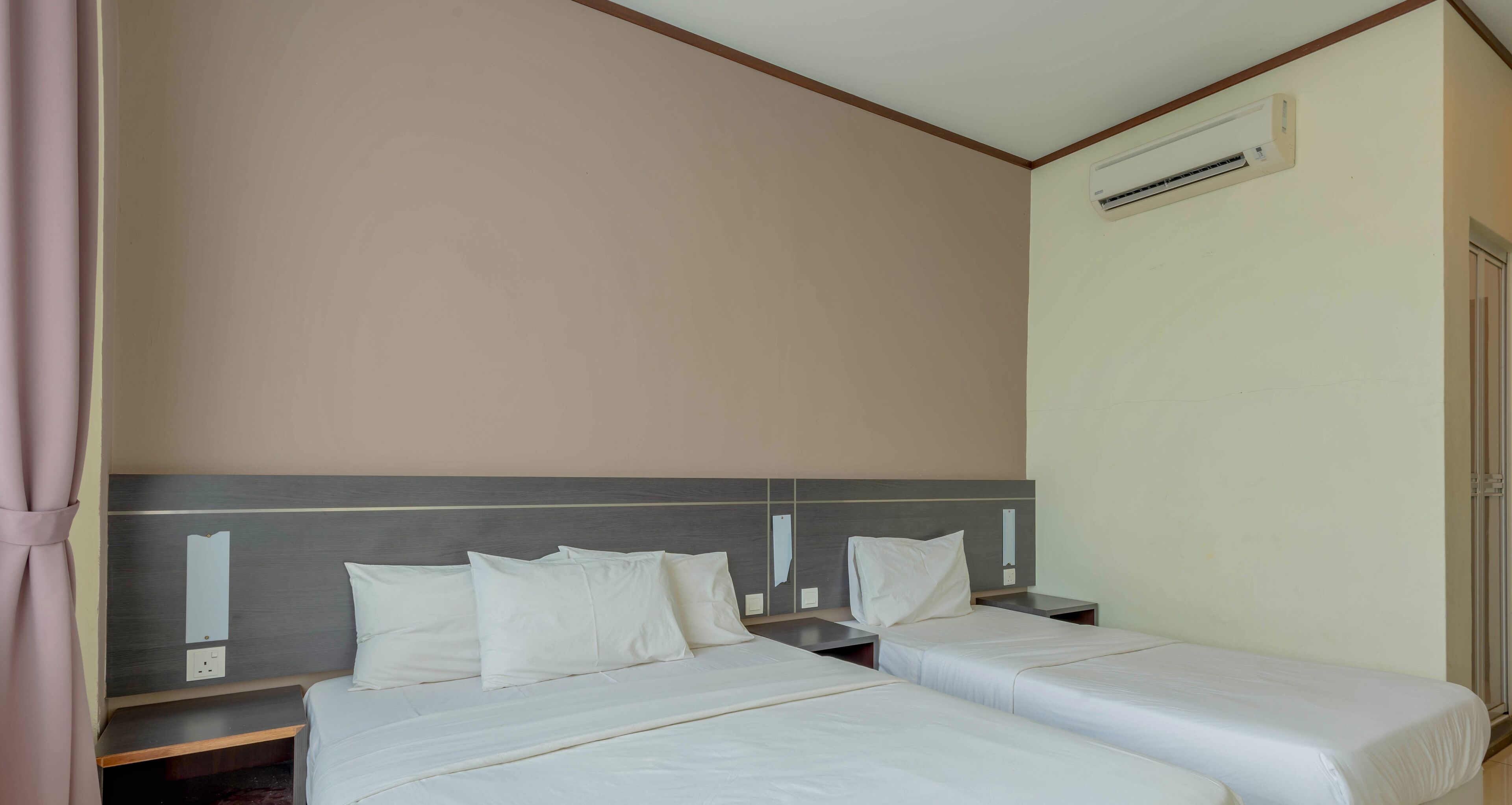 A hotel room with two beds, a wooden headboard, a wall-mounted air conditioner, and a door on the right.