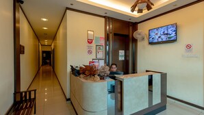 A hotel reception area with a curved reception desk, a television mounted on the wall, and a wooden bench along the corridor. - Kesang Laut Hotel (Muar)