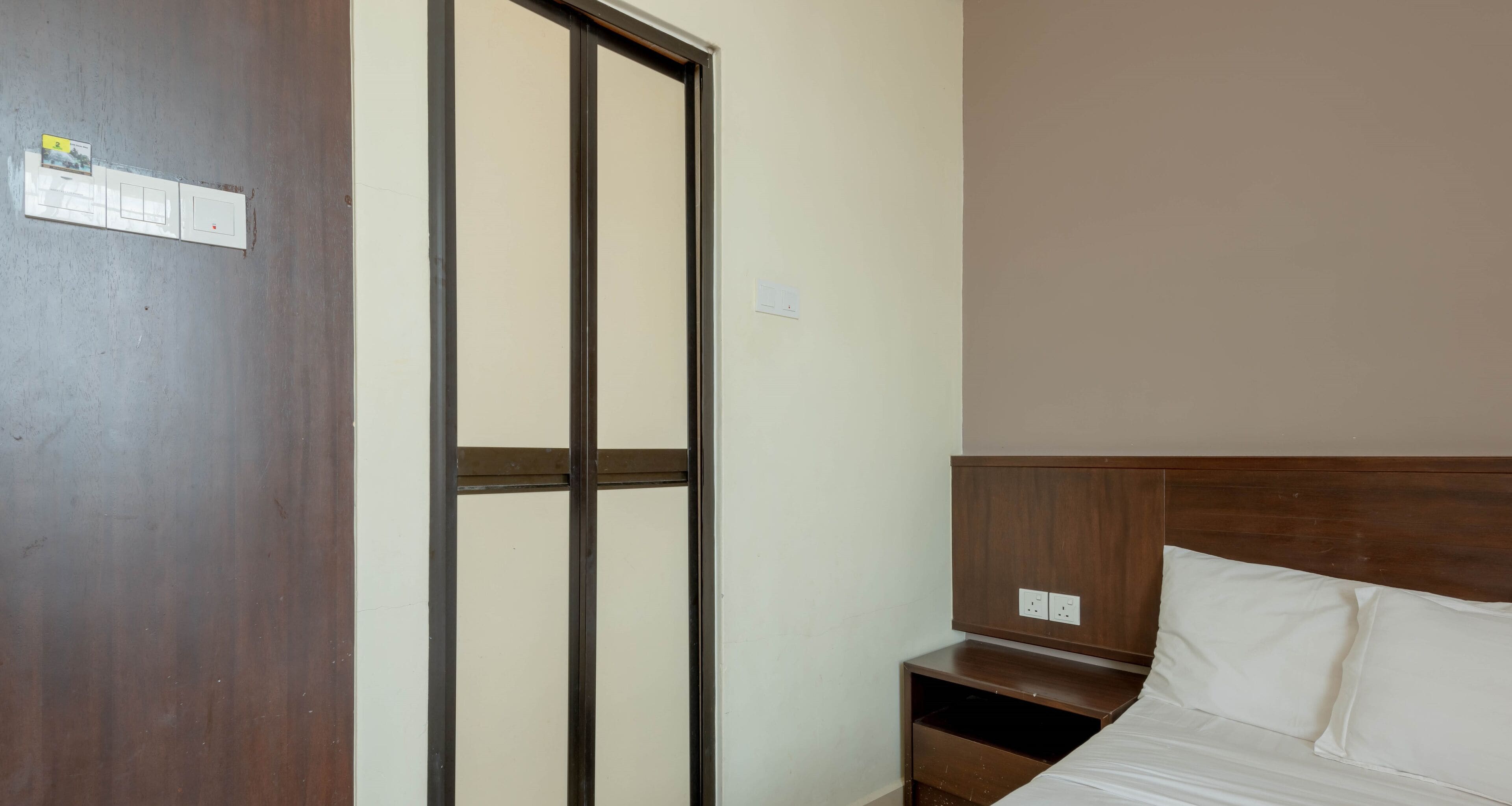 A hotel room with a wooden headboard, a bed with white linens, a nightstand, and a sliding door with a view of the outside.