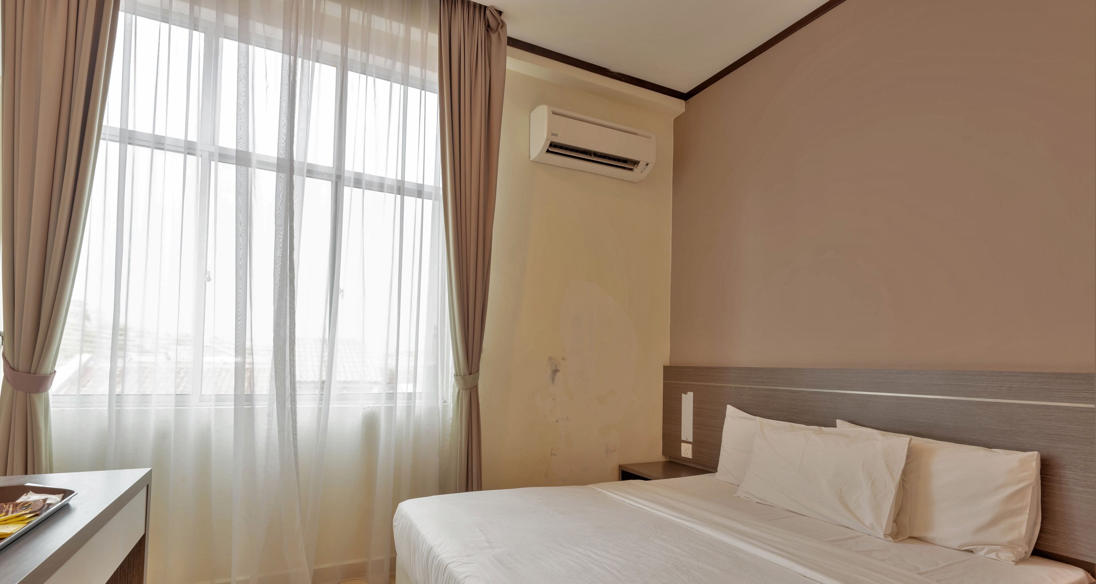 Une chambre d’hôtel avec un lit, une table de chevet, un appareil de climatisation et des rideaux légers.