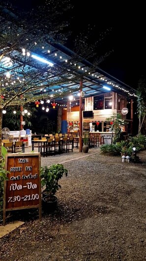 An outdoor seating area with tables and chairs under a covered structure, surrounded by greenery. - Thabli Resort (Kra Buri)