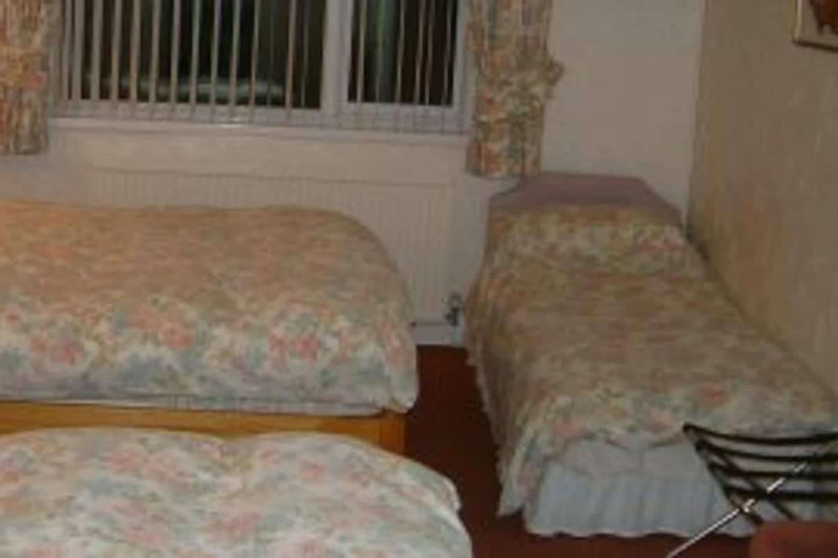 Un dormitorio con dos camas individuales, cabecero de madera, radiador y ventana con cortinas.