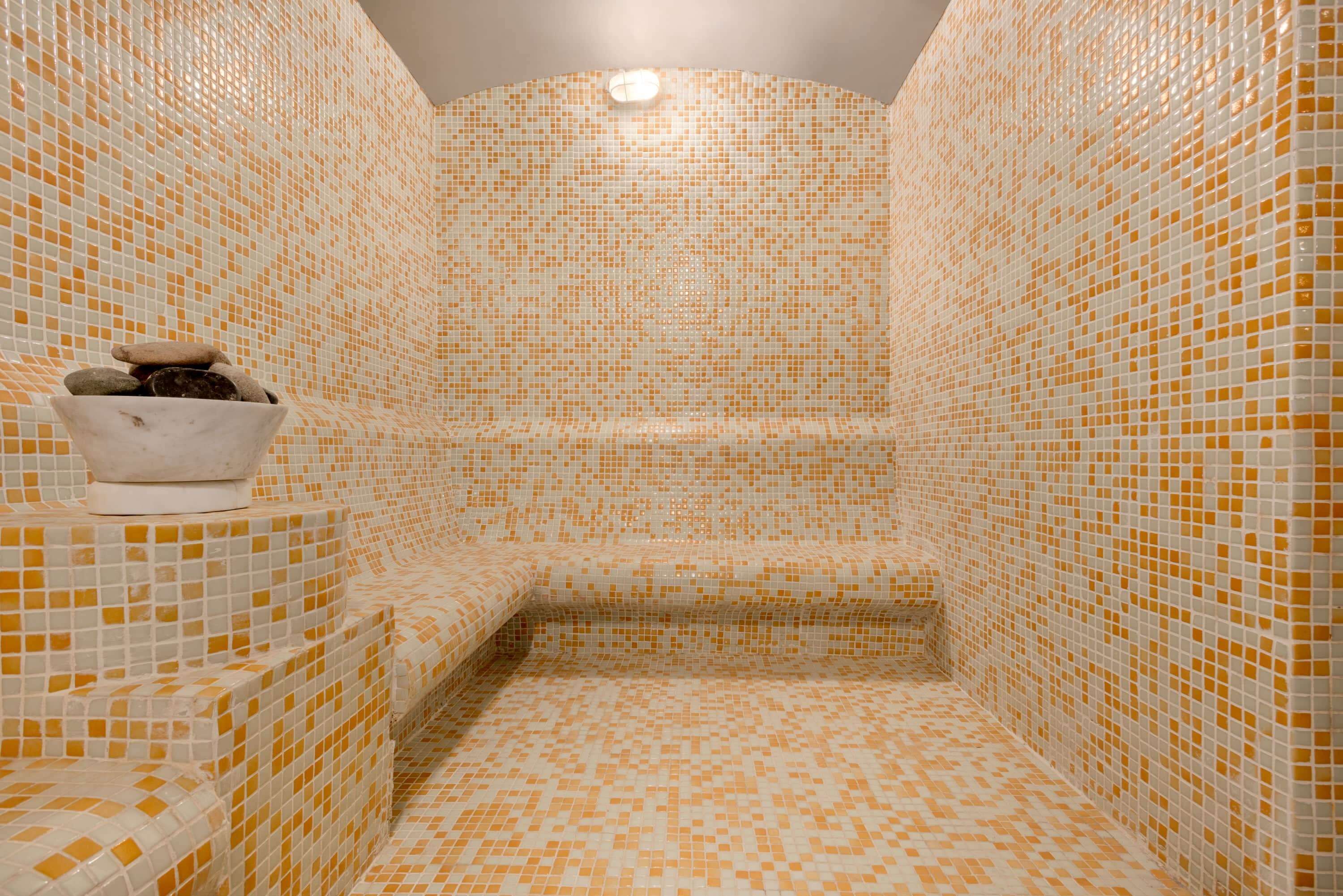 A small, tiled room with a bench and a bowl of stones.