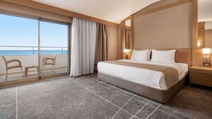 A hotel room with a large bed, a nightstand, a lamp, a sliding glass door leading to a balcony with chairs, and a view of the ocean. - Ramada Resort by Wyndham Unye (Ünye)