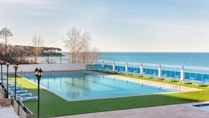 A rectangular swimming pool with a clear blue water surface, surrounded by a green lawn and white lounge chairs. - Ramada Resort by Wyndham Unye (Ünye)