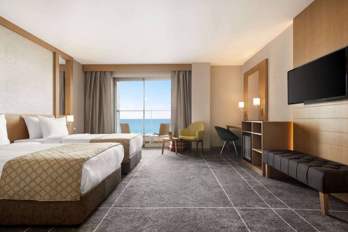 Habitación de hotel con dos camas, un escritorio, una silla, un televisor y vista al océano.