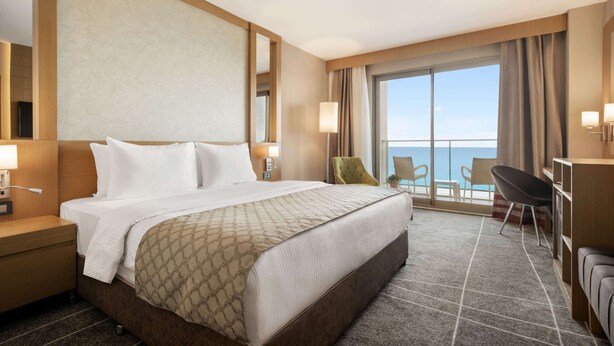A hotel room with a large bed, a desk, a chair, and a view of the ocean. - Ramada Resort by Wyndham Unye (Ünye)