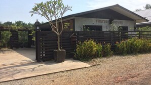 A building labeled "FRUITS HOUSE" with a gated entrance, a small tree in a pot, and a gravel path leading to the gate.