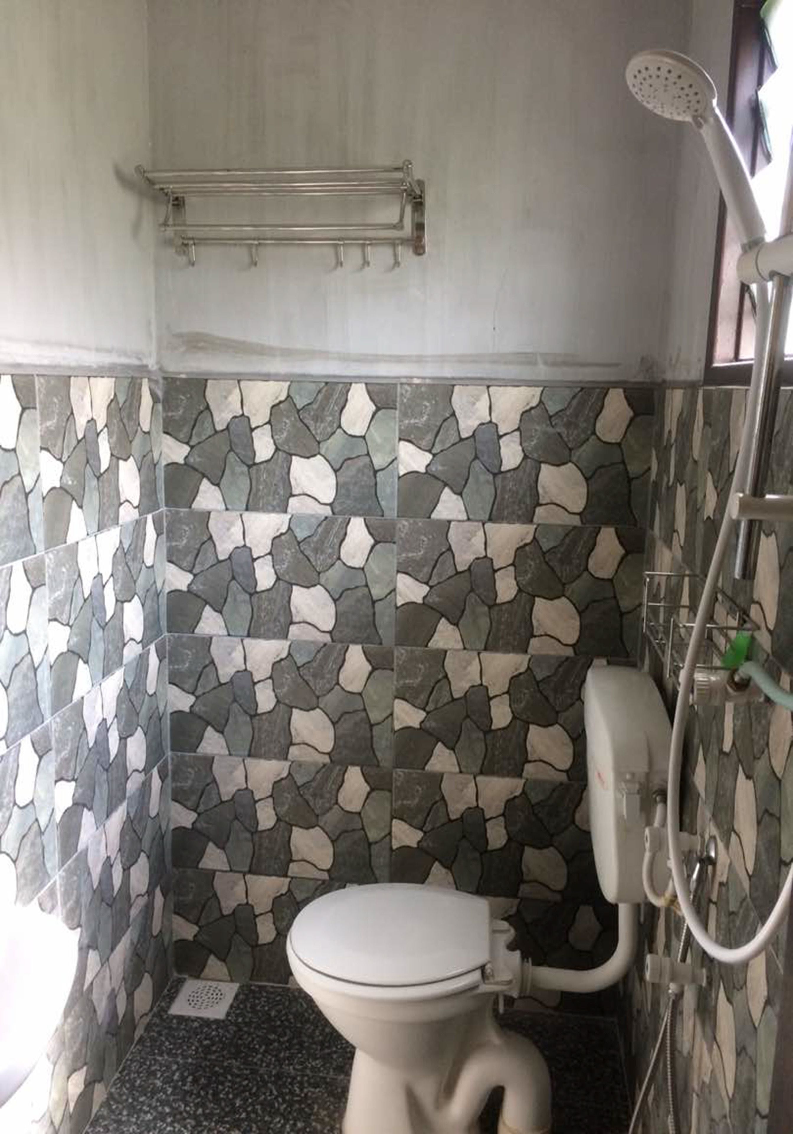 Een kleine badkamer met toilet, douche en een muur met een stenen patroon.